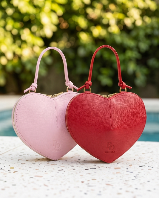 Comparison shot of the pink and red Bulda heart-shaped leather handbags on a white speckled surface.