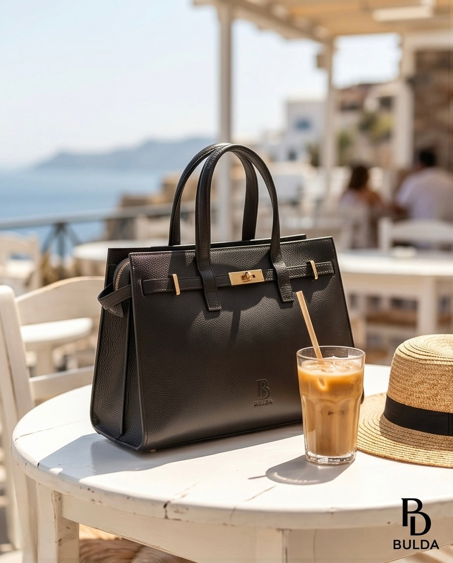lack leather Bulda handbag displayed on a cafe table with a sea view in the background.