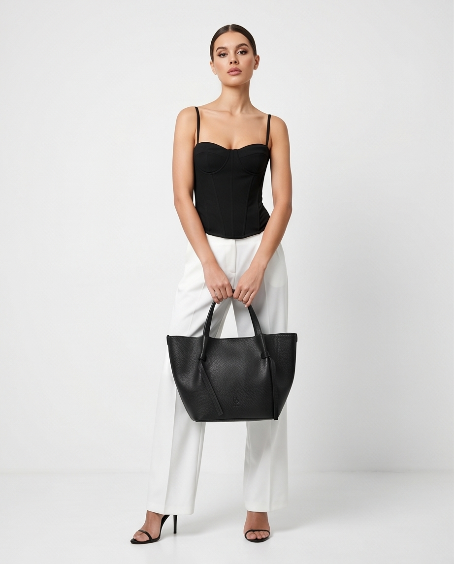 Model holding a black leather tote bag against a clean white background.