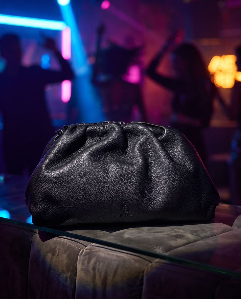 The black soft leather clutch bag by Bulda under neon lights in a fashionable European night club.