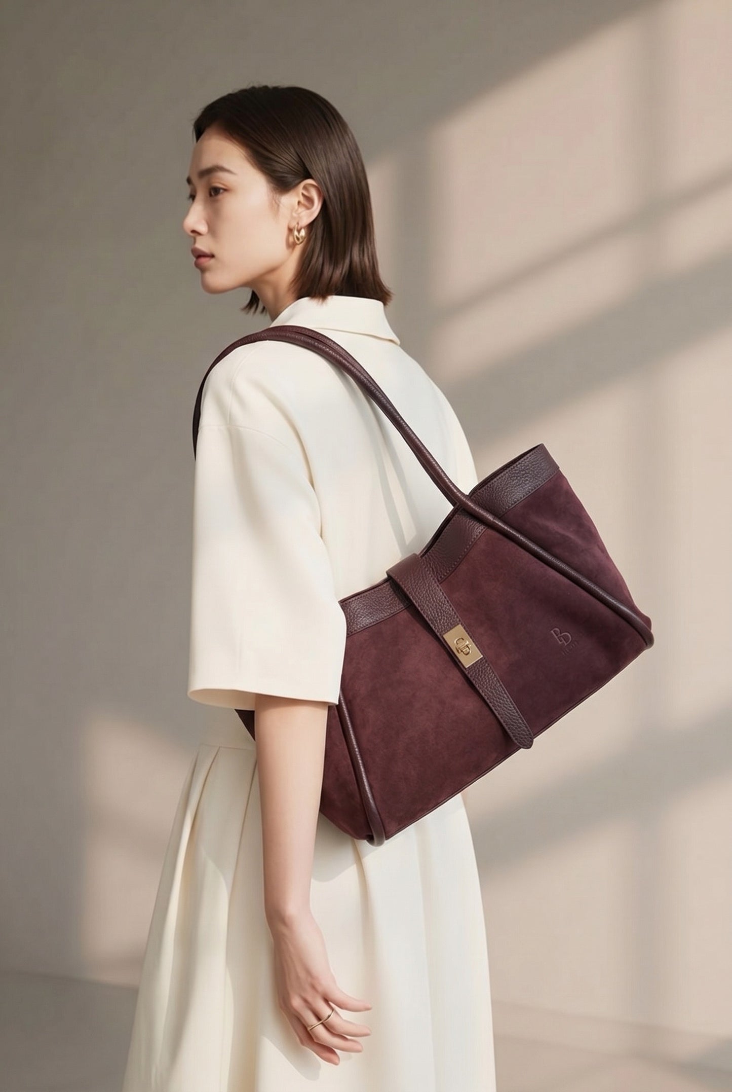 Side view of a model in white attire wearing the BULDA burgundy tote over the shoulder.