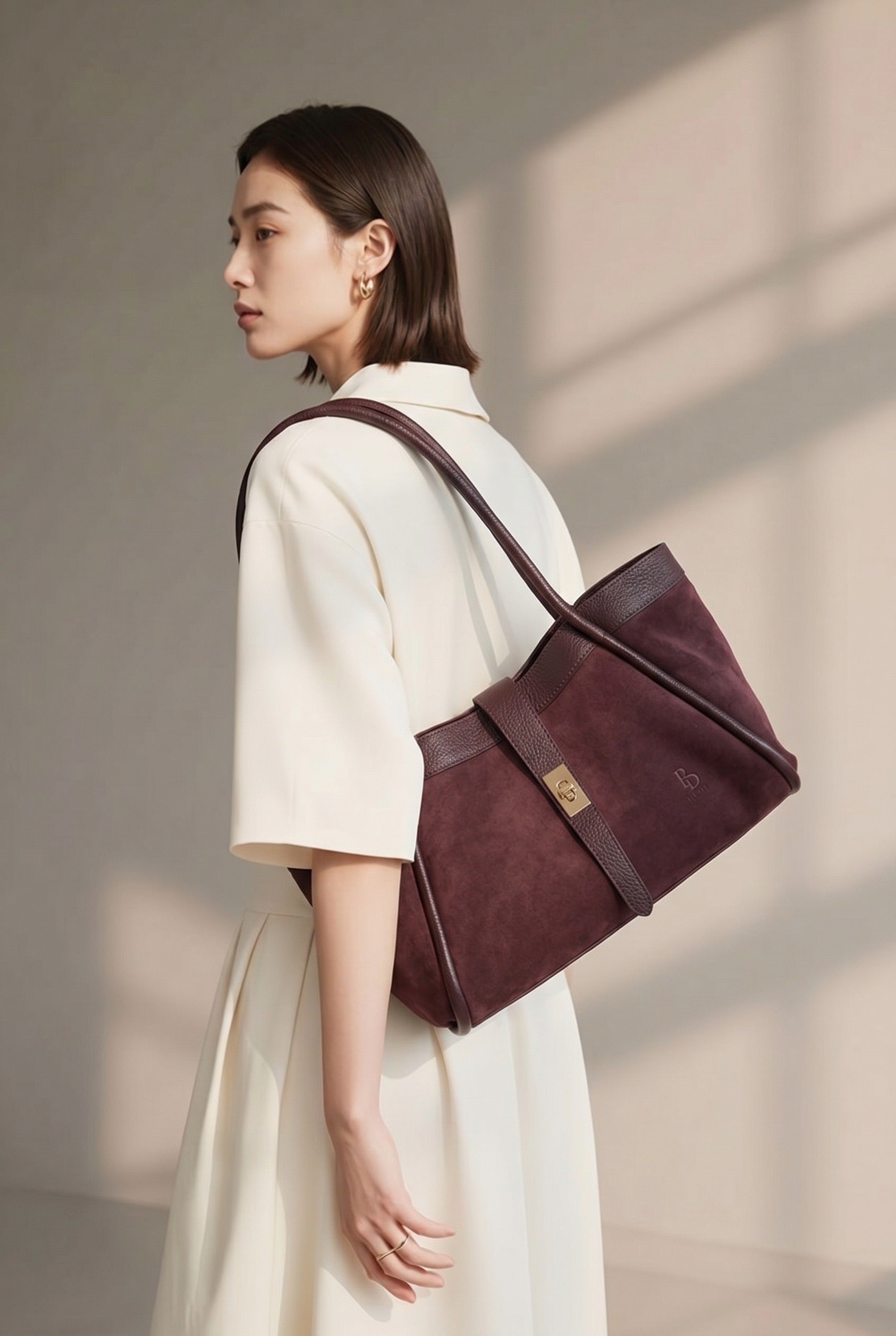 Side view of a model in white attire wearing the BULDA burgundy tote over the shoulder.