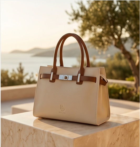 Front view of a cream leather tote bag with brown leather accents in a sunny outdoor setting.